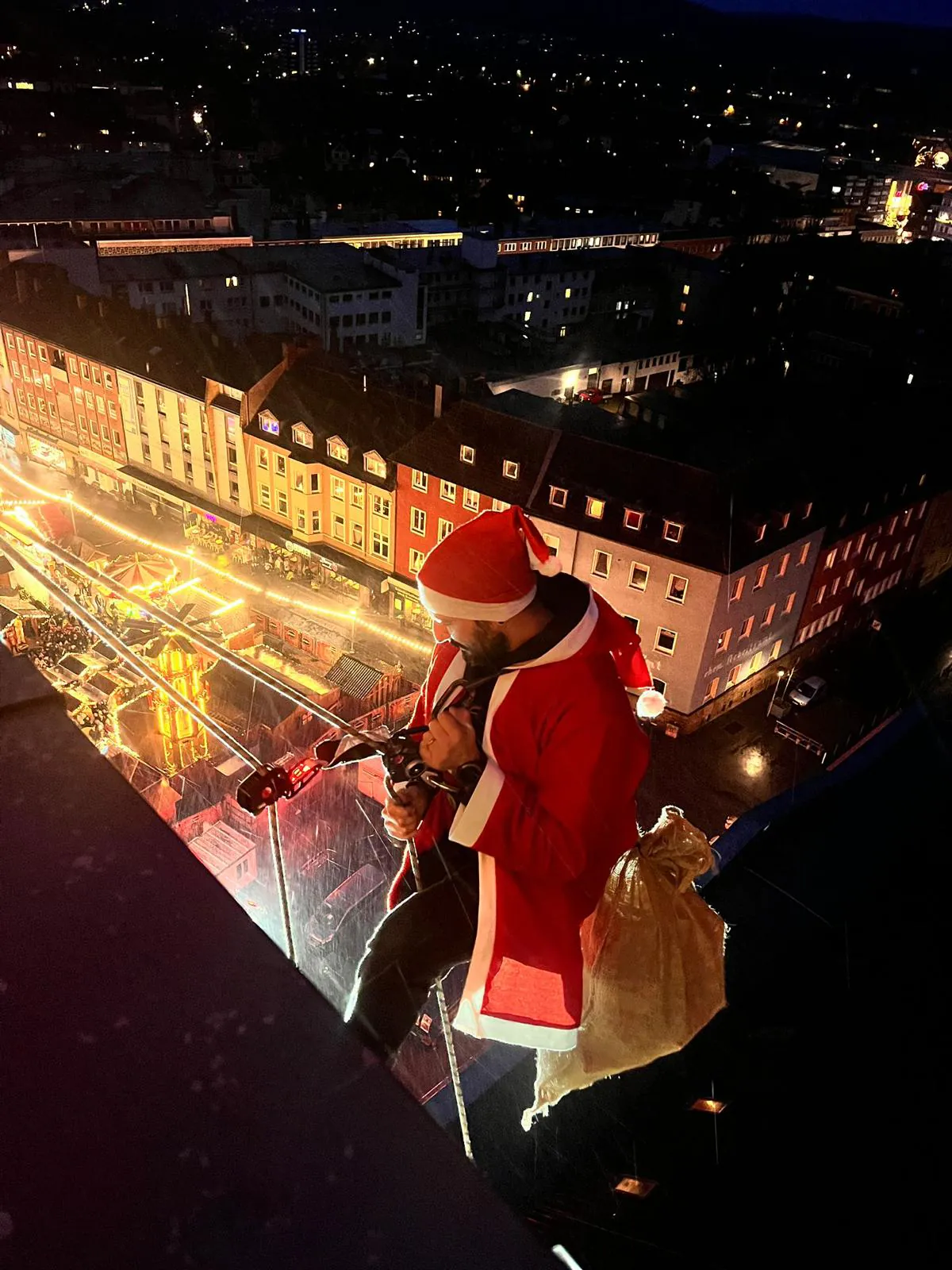 Als Nikolaus verkleideter Industriekletterer seilt sich über dem Weihnachtsmarkt ab